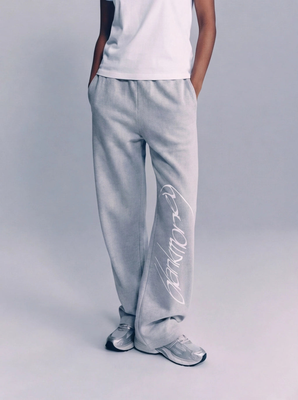 Person wearing light gray pants with a brand logo on a plain background
