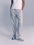 Person wearing light gray pants with a brand logo on a plain background